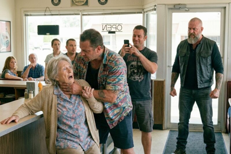 They grabbed an elderly woman by the throat to force her son out of hiding, laughing as they threatened the helpless mother in front of everyone — never imagining the man they were trying to intimidate was already standing right behind them. What looked like a cruel setup against a fragile old lady turned into a chilling moment of reckoning when the room fell silent, boots stopped moving, and the feared Hells Angels boss finally stepped forward. In seconds, the smug faces of the thugs drained of color as they realized too late that the woman they used as bait was protected by the one man nobody in that town dared cross.